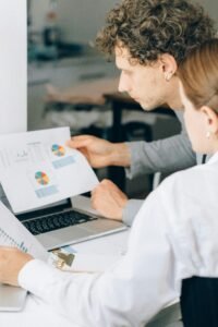 pexels photo 8062287 8062287 Two business professionals reviewing financial charts and graphs in a modern office setting.